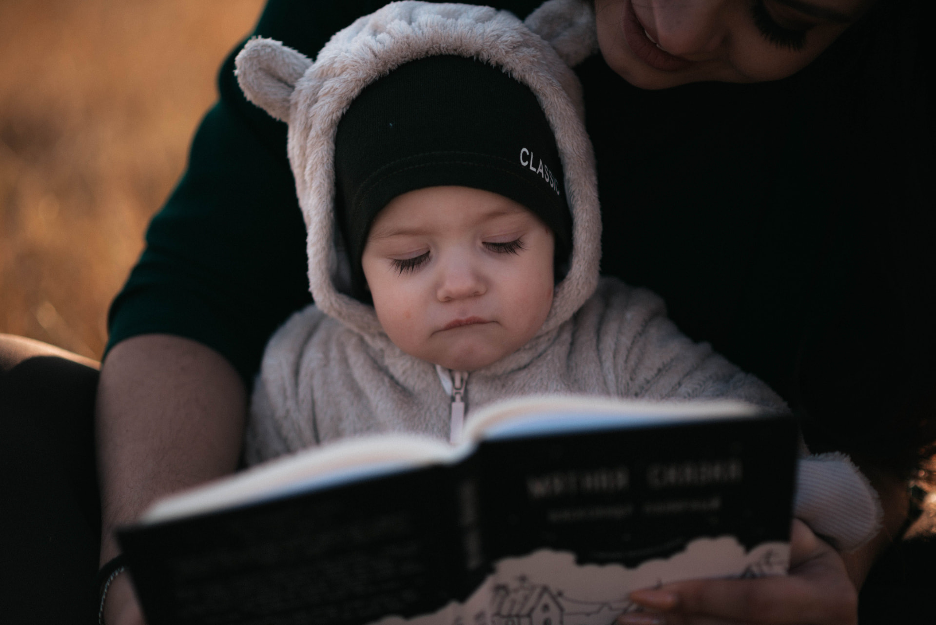 A bundled-up baby looking at a book