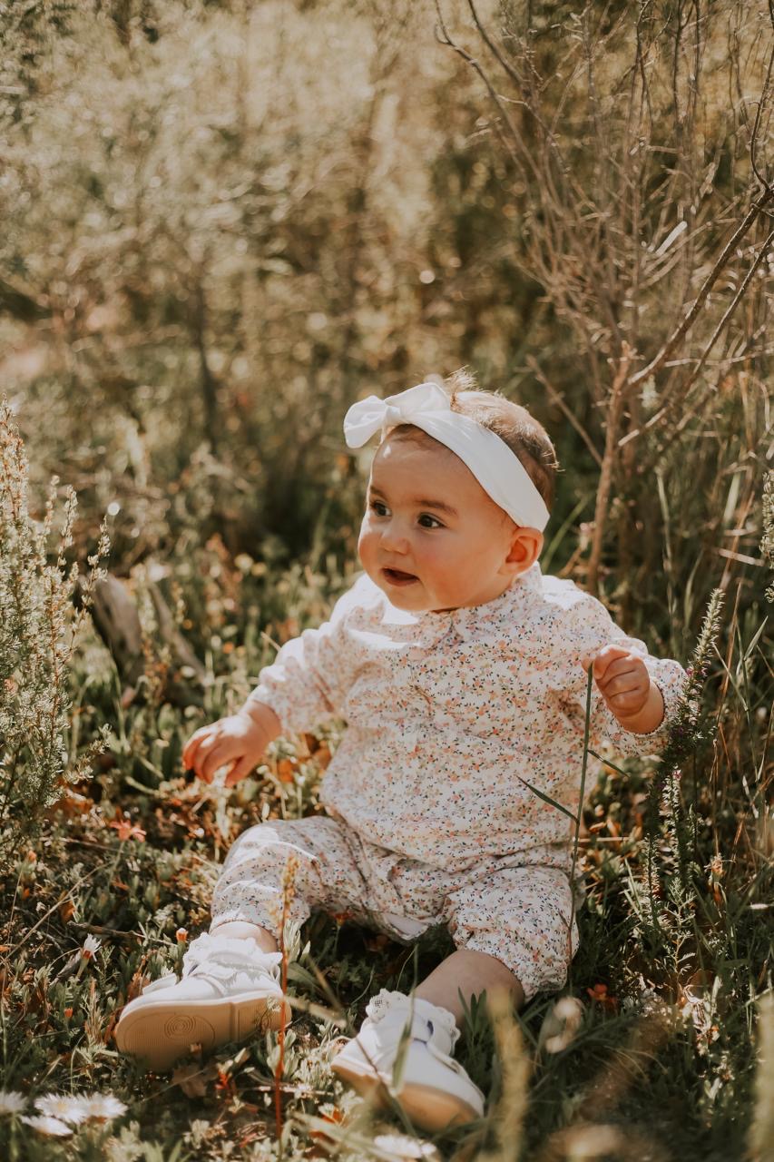 A baby sitting among flowers in a sunlit field